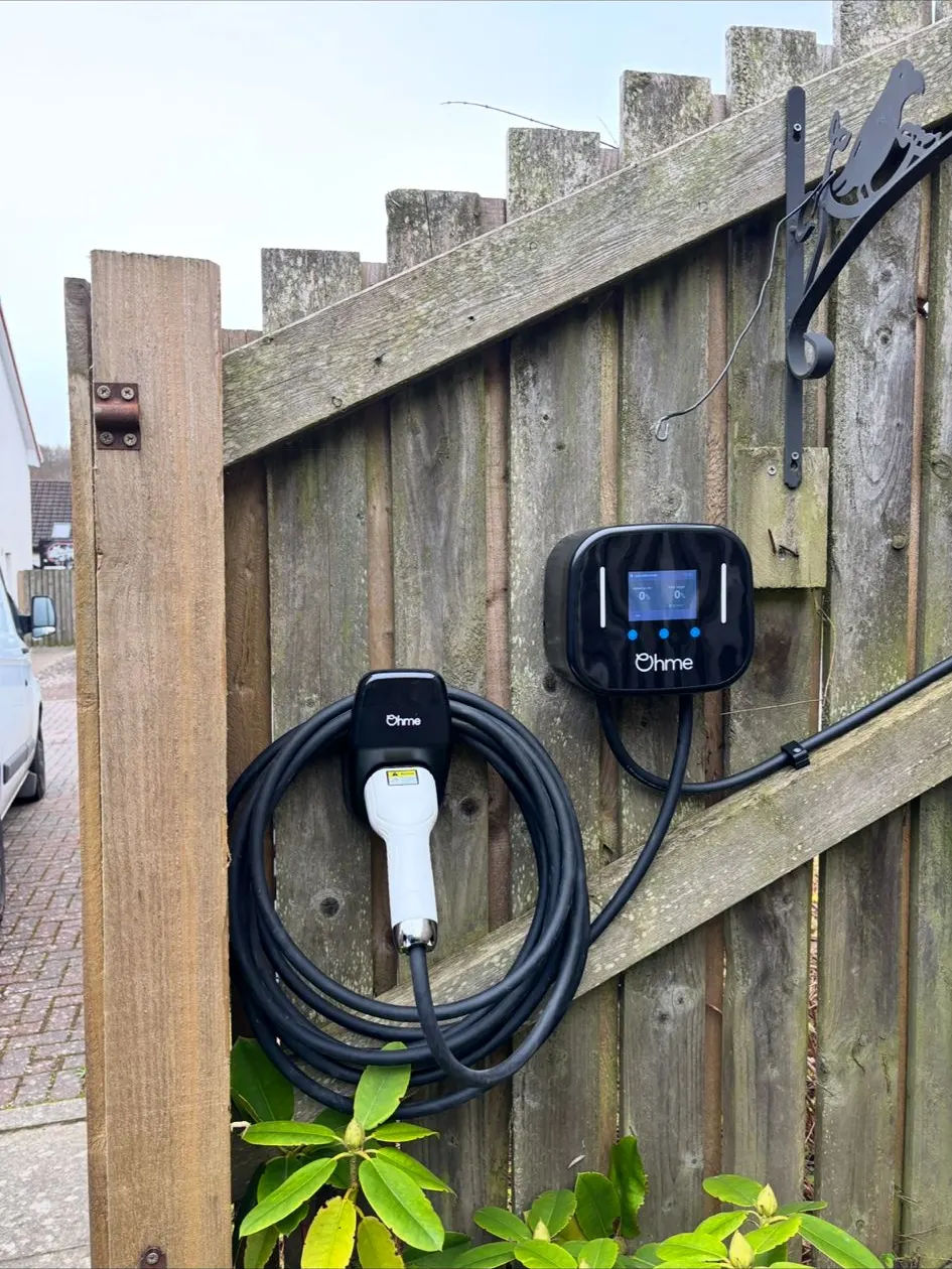 Tethered EV charge point with coiled cable on a garden fence