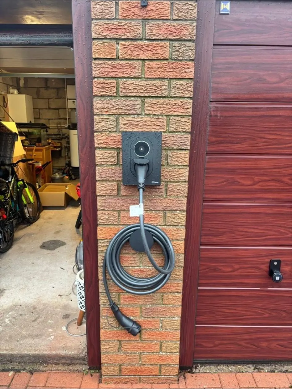 Tethered charge point on a brick pier beside a garage